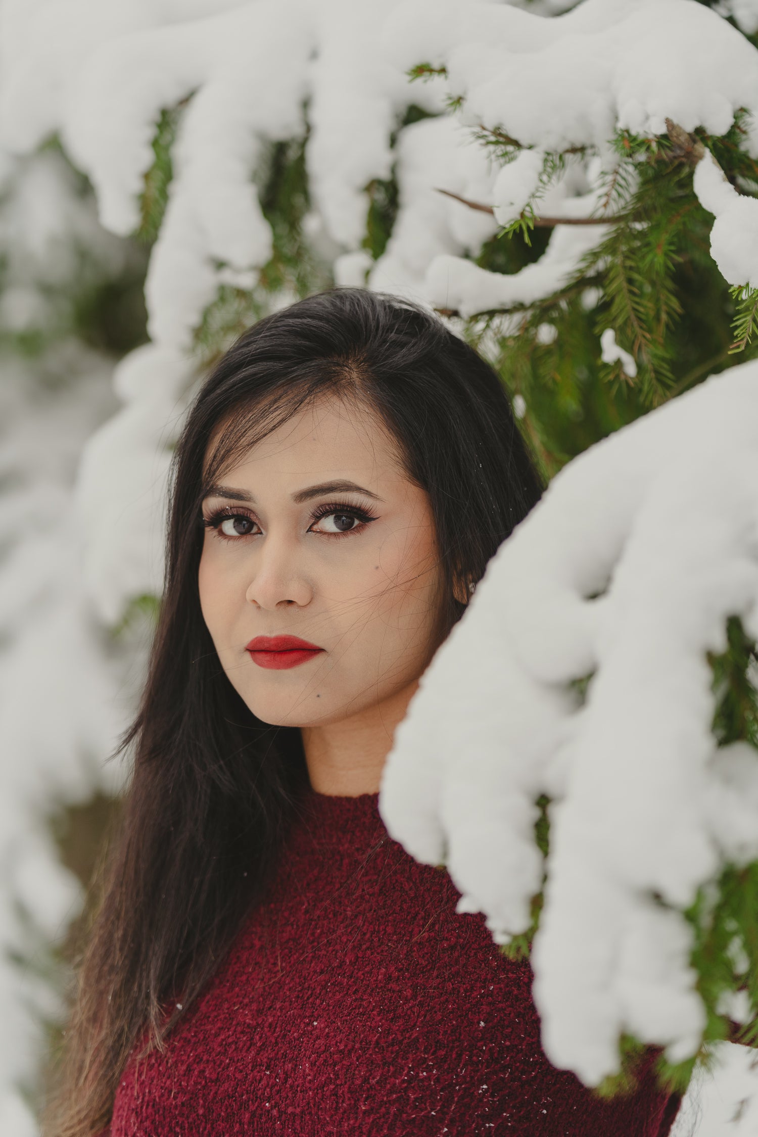 A woman in a red sweater stands before snow-covered trees